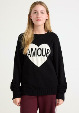 Musta neulepaita, jossa on valkoinen sydän ja sana "AMOUR" paksuilla mustilla kirjaimilla. Valmistettu neulottu materiaali, jossa on ribbatut hihansuut ja helma.