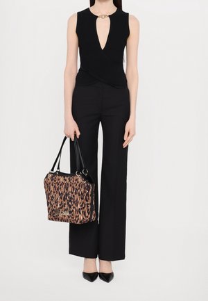 Femme portant un haut noir sans manches avec un col en forme de trou de serrure, un pantalon large noir, des talons noirs, tenant un sac à main imprimé léopard.
