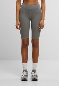 Graue, hoch taillierte Radshorts aus dehnbarem Material mit glatter Textur und kontrastierenden Nähten. Tragen Sie sie mit hellgrauen Turnschuhen und Socken.