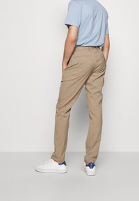 Pantalones chinos beige con un ajuste entallado, con bolsillos traseros y una textura suave, combinados con zapatillas blancas y una camiseta azul claro.