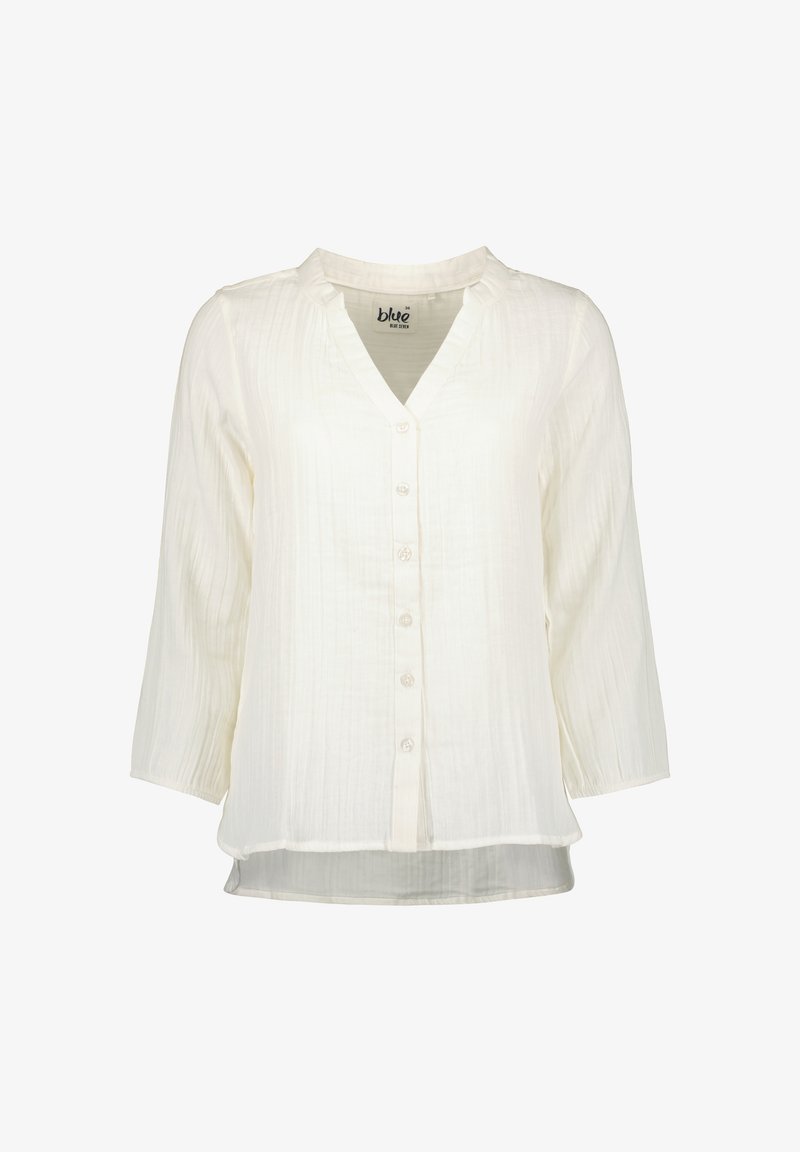 Blouse blanche à manches longues en tissu texturé, col en V, boutonnage sur le devant, et ourlet légèrement arrondi.