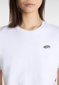 Hvid bomulds t-shirt med rund hals, korte ærmer, med et lille sort "Vans Off the Wall" logo på venstre bryst.