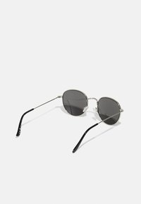 Occhiali da sole rotondi con lenti scure, montatura in metallo argento e aste in acetato nero. Presentano cuscinetti per il naso regolabili e un design minimalista.