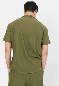 Olivengroene shirt met korte mouwen, gemaakt van ribbelstof, met een kraag, een ontspannen pasvorm en een achterkant met zakdetails.
