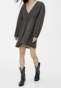 Czarna sukienka w kwiatowy wzór z długimi rękawami, dekoltem w serek i luźnym krojem. Noszona z czarnymi kowbojkami z srebrnymi akcentami.