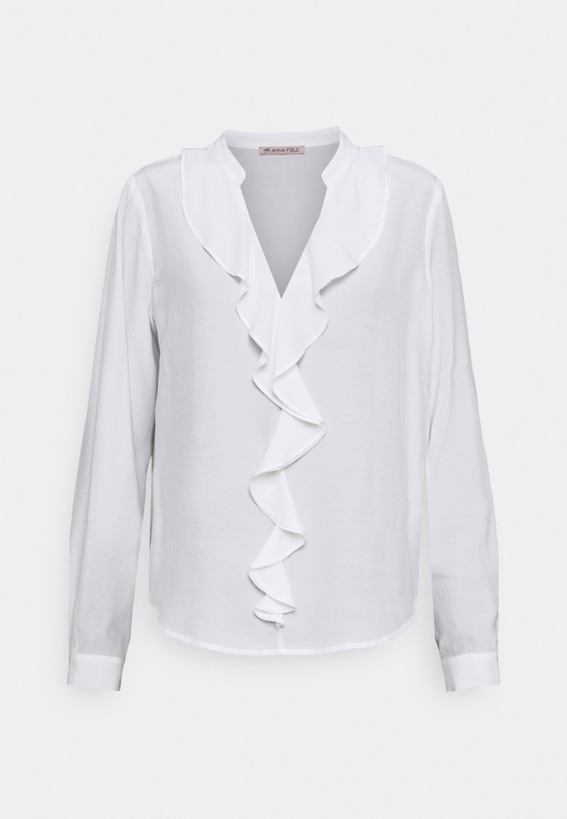 Chemisier blanc à manches longues avec un décolleté en V et des détails froncés sur le devant. Fabriqué dans un tissu lisse avec une texture légèrement translucide.