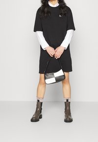 Robe t-shirt noire oversize, chemise blanche en dessous, sac à main noir et blanc, bottes à hauteur de genou brillantes, chaussettes rayées rose et blanche.