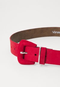 Cintura in suede rosso con fibbia quadrata, hardware in argento e superficie interna liscia. Presenta fori regolabili lungo la cintura per la variazione delle dimensioni.