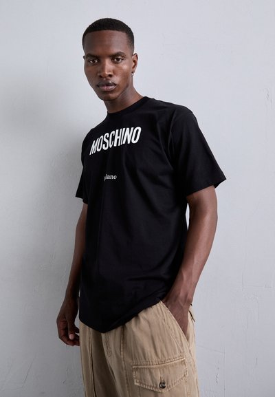 Must musta T-särk, kus on julged valged "MOSCHINO" kirjad ja väiksem "Milano" logo. Lühikesed varrukad, lõdva lõikega, sile tekstuur.