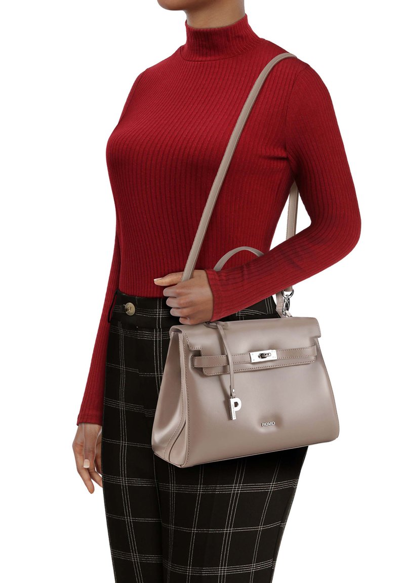 Sac à main en cuir beige avec une forme structurée, une poignée supérieure et une bandoulière amovible. Présente une étiquette logo et des accents métalliques argentés.