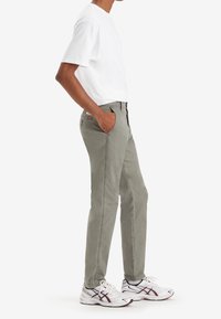 Jasnoszare bawełniane spodnie o dopasowanym kroju, wyposażone w boczne kieszenie i naszywkę z logo. Zestawione z białym T-shirtem i białymi sneakersami.