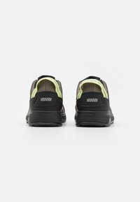 Chaussures de sport noires avec une tige texturée, des accents en maille et un détail réfléchissant en néon vert au niveau du talon. Semelle en caoutchouc épaisse pour le soutien.
