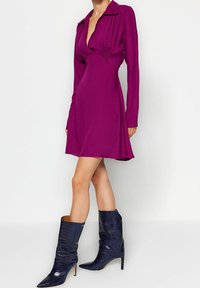 Tajt och långärmad klänning i livfull magenta med djup V-halsringning och plisserade detaljer. Matchad med glänsande, marinblå stövlar med krokodilsmönster.