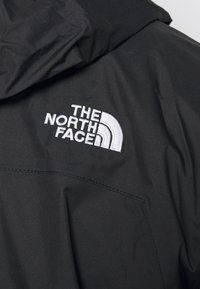 Czarna kurtka techniczna z białym, haftowanym logo "The North Face" oraz gładkim, matowym wykończeniem tkaniny.