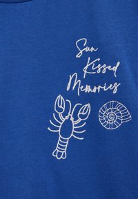 Tissu bleu avec texte brodé en blanc "Souvenirs Ensoleillés" accompagné d'un homard et d'un motif de coquillage en spirale.