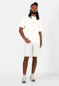 Kortärmad krämfärgad t-shirt med en liten röd logo, i kombination med vita denimshorts som har fem fickor och silverdetaljer.