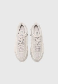 Para jasnobeżowych sneakersów Nike Shox z sznurówkami, widziana z góry na jednolitym białym tle.