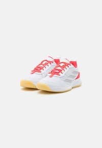 Sneakers feature a white mesh upper with red laces and accents, silver branding detail, and a textured yellow rubber sole.