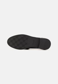 Suela de zapato de goma negra con un patrón texturizado y un logo, bordes lisos y ligera elevación en el tacón. Banda de rodadura transparente para mayor agarre.