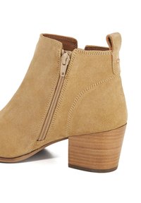 Tan suede ankle boot with a side zipper, a stacked wooden heel, and a slightly rounded toe. Smooth texture and simple seam detailing.