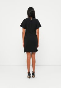 Schwarzes Kurzarmkleid mit einem Schlitz im Rücken, figurbetonter Schnitt und knielanger Saumlänge, kombiniert mit schwarzen High-Heels.