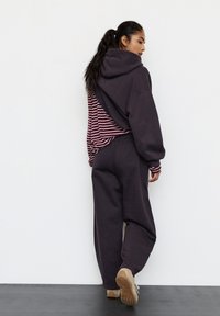 Hanorac oversize mov închis cu dungi pe spate, asortat cu pantaloni largi și adidași bej. Design simplu și croială lejeră.