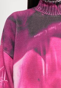 Pull en laine à col montant dans des nuances de rose et de gris foncé, avec un motif abstrait et flou.