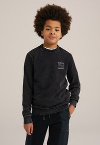 Schwarzes Baumwoll-Sweatshirt mit Rundhalsausschnitt, gerippten Bündchen und einem rechteckigen, gestreiften Taschen-Detail auf der linken Brust. Verwaschene Textur.