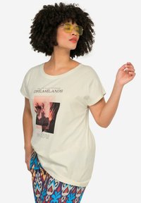 Camiseta beige clara con cuello redondo, que presenta una impresión gráfica en rosa y negro. Tejido de algodón suave y ligero.
