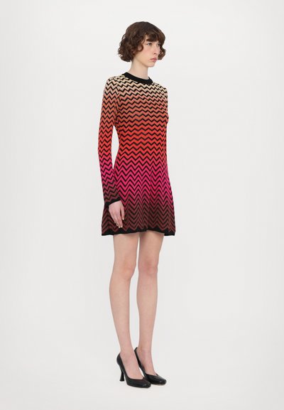 Vestido de mangas longas com um padrão zigzag em gradiente, em tons vibrantes de laranja e rosa, com um acabamento preto e um design ajustado.