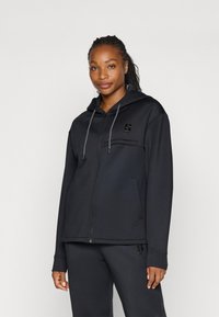 Sudadera con cremallera negra hecha de felpa suave, con un bolsillo frontal, capucha con cordón y un acento de logo en el pecho. Presenta puños de canalé.
