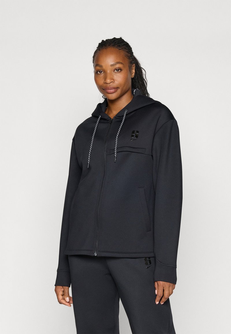 Sudadera con cremallera negra hecha de felpa suave, con un bolsillo frontal, capucha con cordón y un acento de logo en el pecho. Presenta puños de canalé.