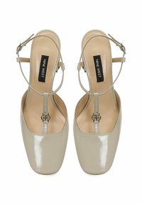 Talons slingback en cuir verni beige avec orteil carré, bride à la cheville et semelle intérieure signée. Design minimaliste avec une finition brillante.