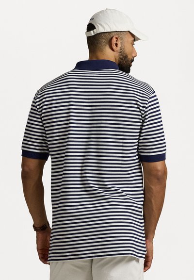Marineblå og hvitstripet polo skjorte med ribbet krage. Korte ermer, strukturert stoff, sidesplitter og detaljert finish. Bakvisning vist.