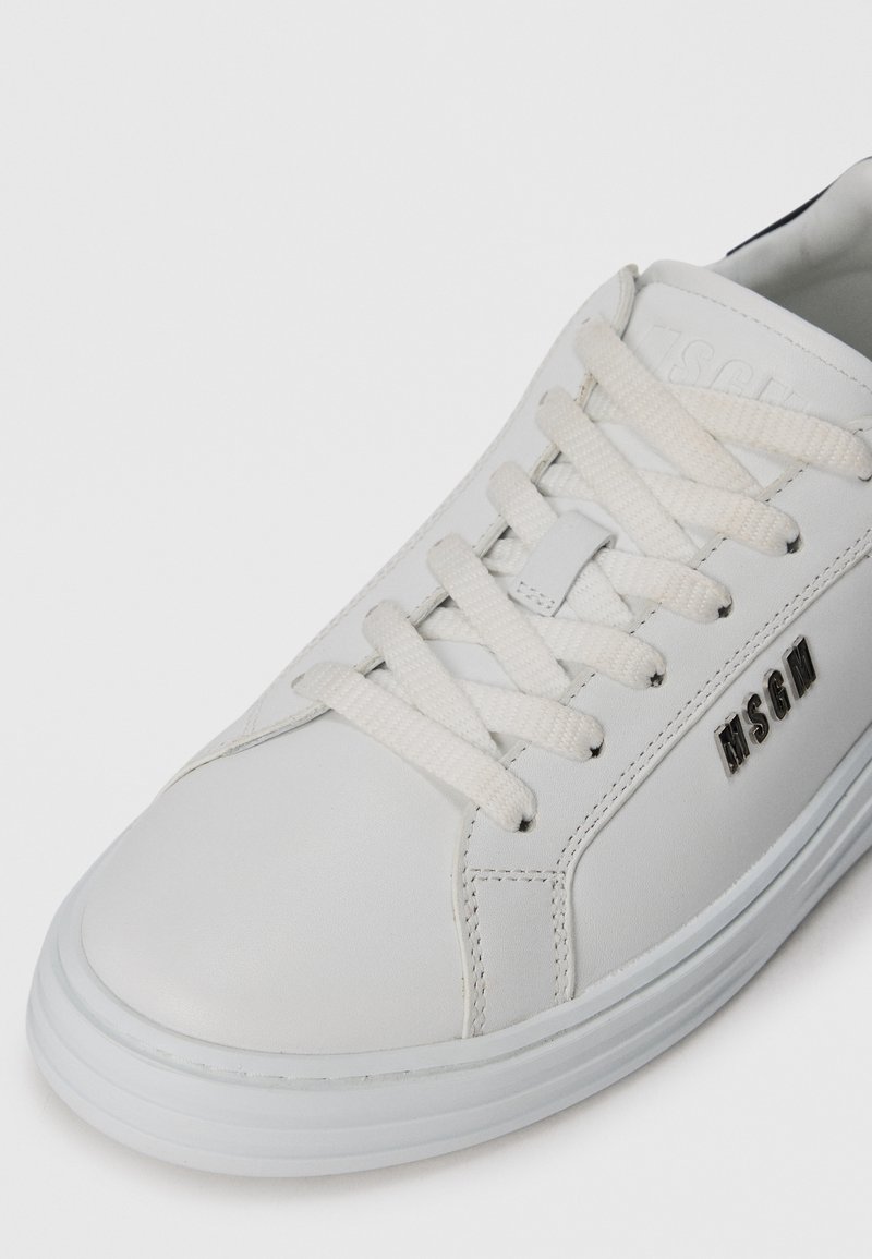 Baskets en cuir blanc avec lacets blancs et logo métallique MSGM sur le côté, dotées d'une épaisse semelle blanche et de détails cousus.