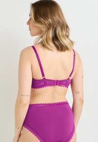 Reggiseno magenta con pizzo e culotte a vita alta, caratterizzati da spalline regolabili e chiusura a gancio sul retro, con una texture di tessuto liscia.