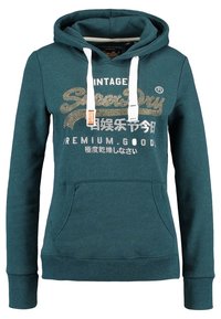 Felpa color teal con cappuccio, cordini, tasca frontale e stampa vintage in oro e bianco. Realizzata in tessuto morbido e testurizzato, con polsini a costine.