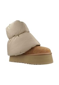 Bota estilo plumón en color beige con punta de ante suave y suela de plataforma redondeada. Presenta una parte superior acolchada para aislamiento y comodidad.