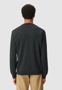 Ciemnoszara, długi rękaw sweter o gładkiej fakturze, okrągłym dekolcie i prążkowanych mankietach, zestawiony z jasnymi spodniami.