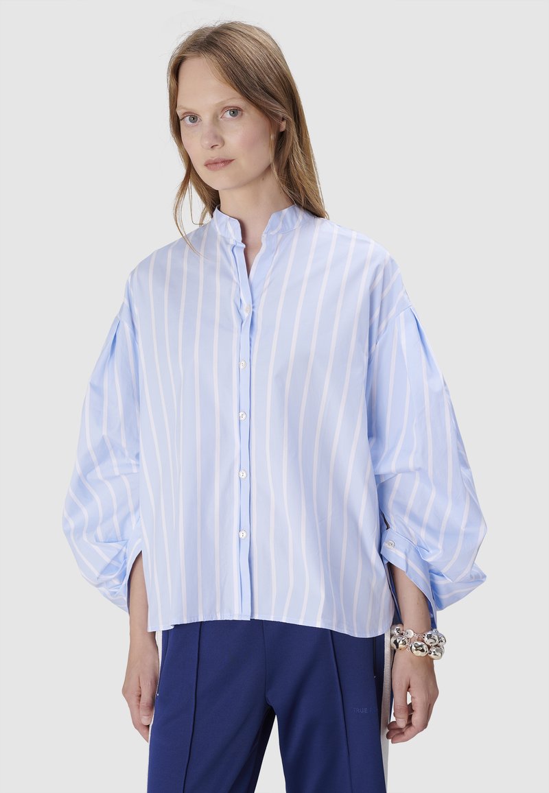 Light blue long-sleeve shirt with white vertical stripes, a stand collar, button closure, and wide, voluminous sleeves.