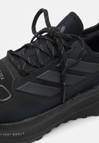 Chaussure de sport noire avec surface texturée, design à lacets et logo à trois bandes. Elle dispose d'une semelle rembourrée étiquetée "LIGHT BOOST."