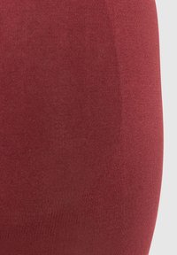 Röd ribbad tyg med en slät struktur, med en figurnära design som följer konturerna och en subtil lyster. Accenter inkluderar konsekvent ribbning.