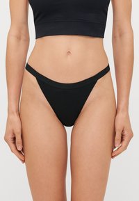 Fekete bikinitop, minimalista tangával, vékony oldalszíjakkal és sima, elasztikus derékpánttal. Puha, rugalmas anyag.