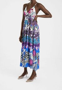 Robe maxi avec un motif floral vibrant dans des teintes de rose, bleu et violet. Présente un décolleté en V profond et de fines bretelles. Une paire de talons embellis.