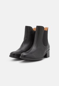 Botines de cuero negro con un acabado suave, paneles laterales elásticos, punta redondeada y tacón cuadrado. Interior forrado con material de color claro.