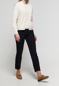 Svetle béžový svetr na knoflíky s kulatým výstřihem a dlouhými rukávy; kombinován s černými úzkými džínami a hnědými mokasínami.