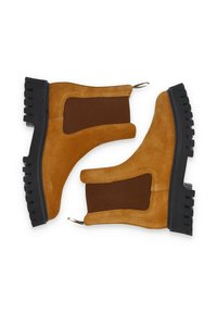 Bottines en cuir suédé marron avec des panneaux latéraux en élastique, une semelle en caoutchouc noir texturé et une languette pour un enfilage facile.