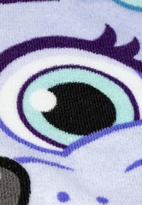 Primo piano di un tessuto in peluche con grandi occhi stilizzati in tonalità di viola, nero e azzurro chiaro, con superficie texturizzata e colori a contrasto.