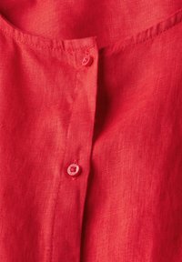 Camicia in lino rosso con un tessuto testurizzato, una placca a mezza bottoni con bottoni rossi e una piccola tasca sul lato sinistro.
