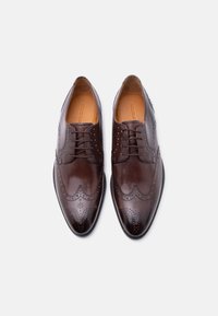 Καφέ δερμάτινα παπούτσια φόρμας με διακοσμητικά λεπτομέρειες brogue, σχέδιο με καπάκι στα δάχτυλα, και ομαλή υφή, με κλείσιμο με κορδόνια και γυαλιστερό φινίρισμα.